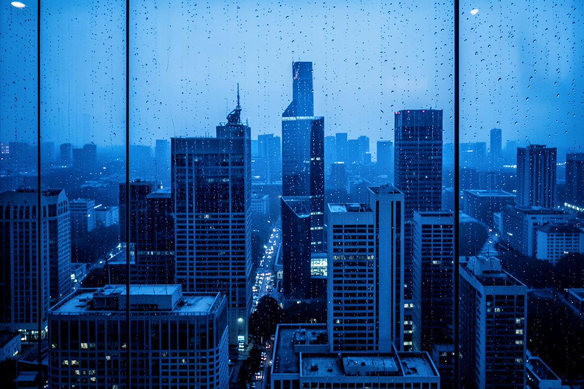 International business district skyline at blue hour behind rain-flecked glass
